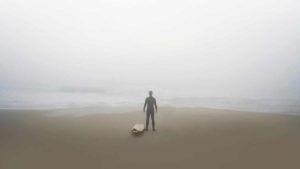 Surfer on beach at dawn looking out at the fog covered ocean